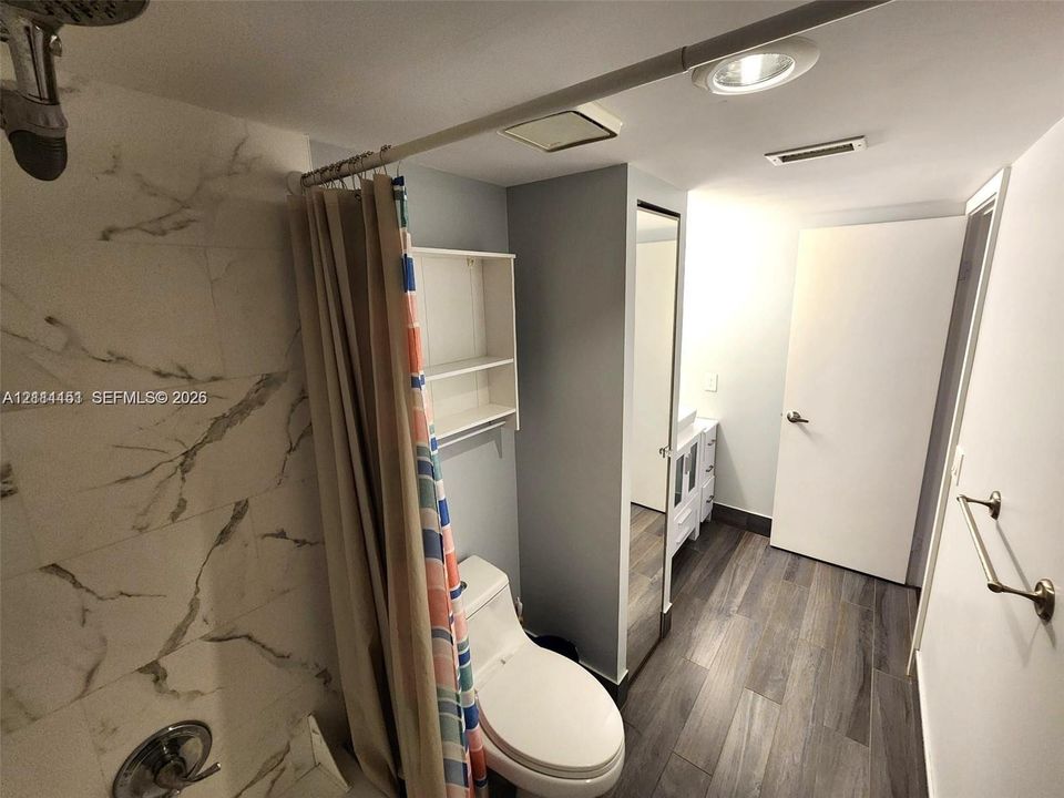 Bathroom featuring shower surround with large-format stone-patterned tile, wood-finish flooring, white vanity, built-in wall shelving, and inset ceiling lighting