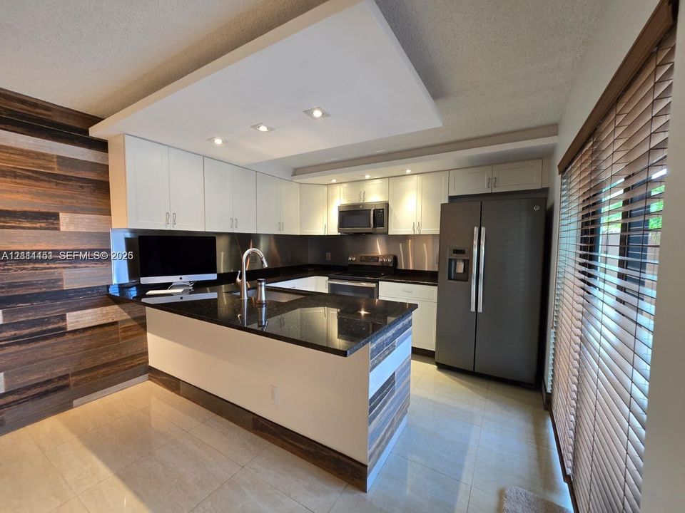 Kitchen featuring white shaker-style cabinetry, dark stone countertops, stainless steel appliances, recessed ceiling lighting, and horizontal wood-panel accent wall