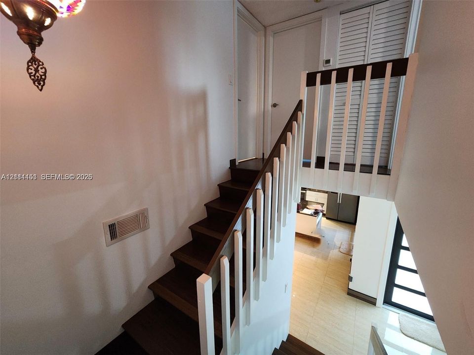 Staircase featuring wood-finish treads, white vertical balusters, and a tiered architectural design with louvered closet doors