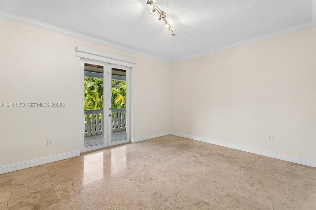 Interior space featuring natural stone tile flooring, crown molding, a multi-bulb track lighting fixture, and French doors opening to an exterior balcony with a stone balustrade