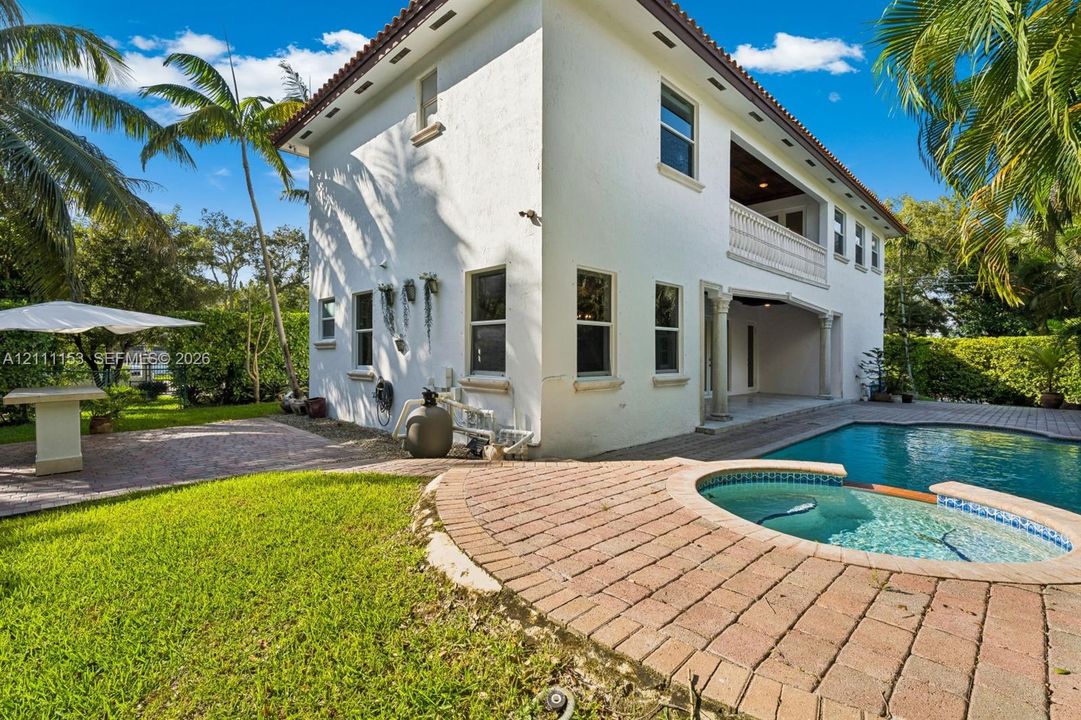 Stucco exterior residence featuring an integrated pool and spa, brick paver patio, second-story balcony, and manicured grounds