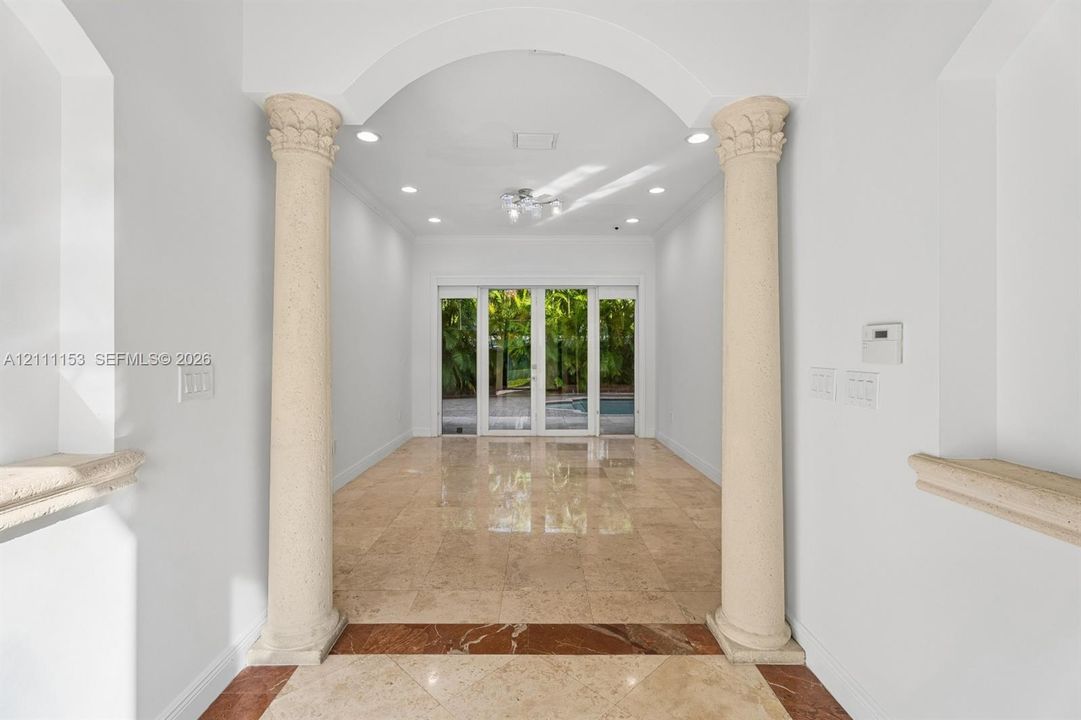 Entryway featuring arched architectural details, decorative stone columns, polished stone flooring with inlaid border, recessed lighting, and glass paneled doors