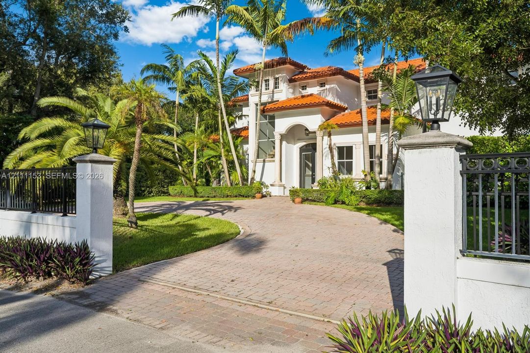 Mediterranean-style residence featuring a terra cotta tile roof, arched entryway with decorative columns, paved driveway, stucco exterior, and gated perimeter wall