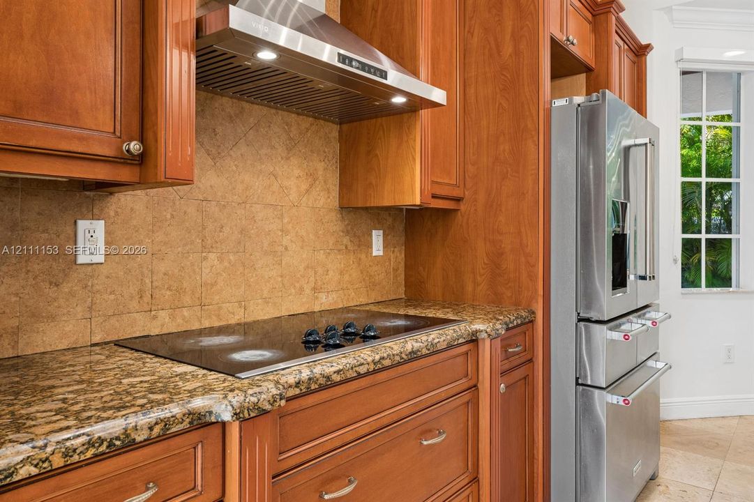 Kitchen featuring wood cabinetry, stone countertops, a glass cooktop, a stainless steel chimney-style range hood, and a stainless steel French door refrigerator