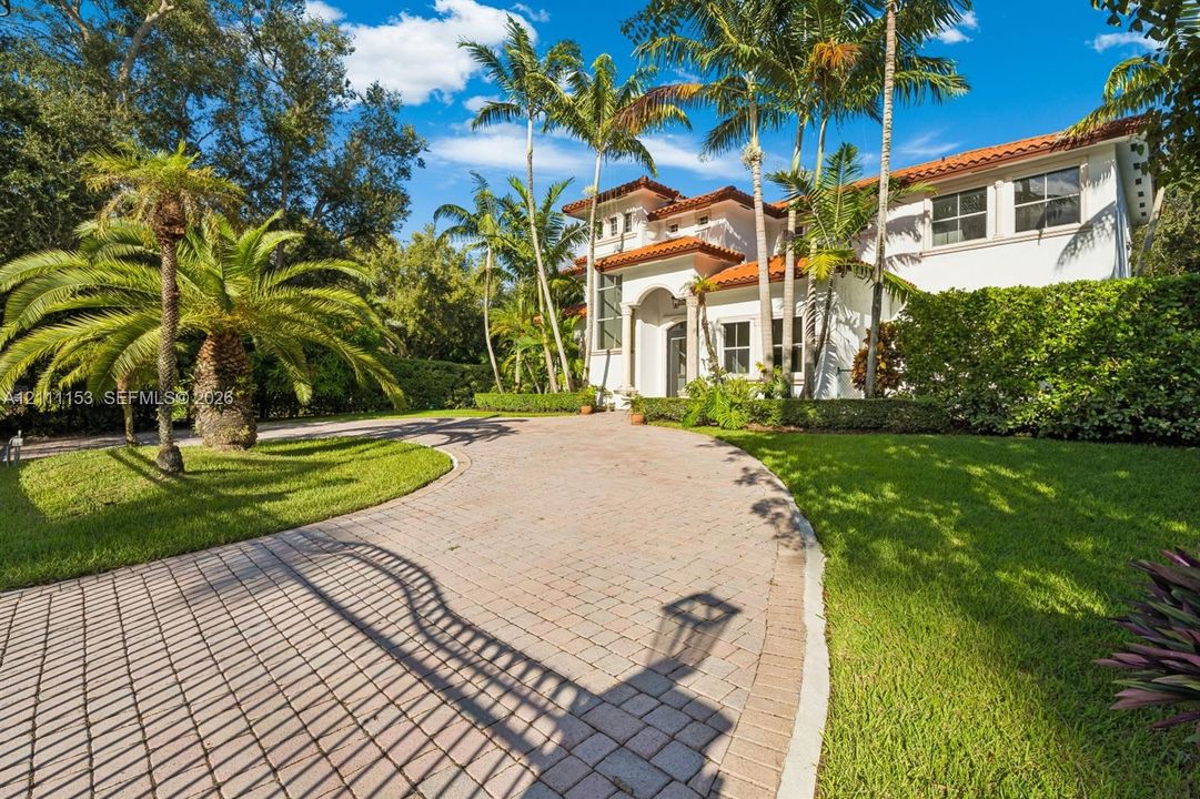 Stucco exterior featuring a terracotta tile roof, arched entryway, paved driveway, and mature palm landscaping