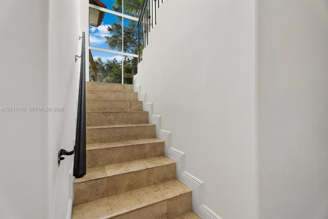 Staircase featuring natural stone treads, wrought iron railing, and floor-to-ceiling windows