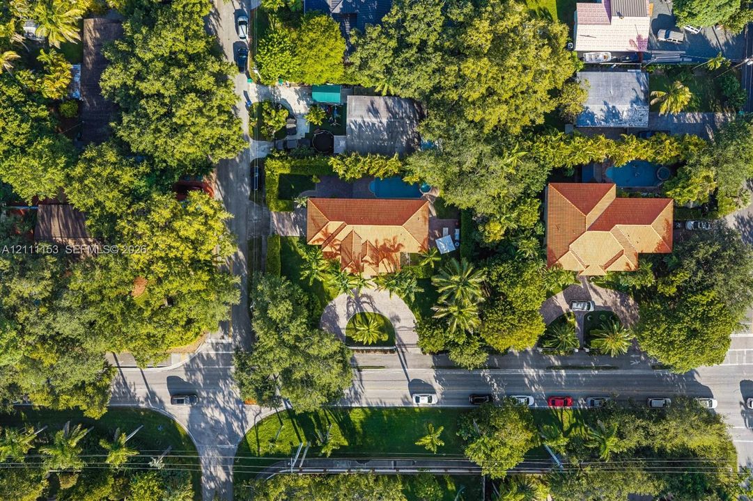 Aerial perspective of a property featuring a tiled roof, circular driveway, swimming pool, and dense perimeter landscaping