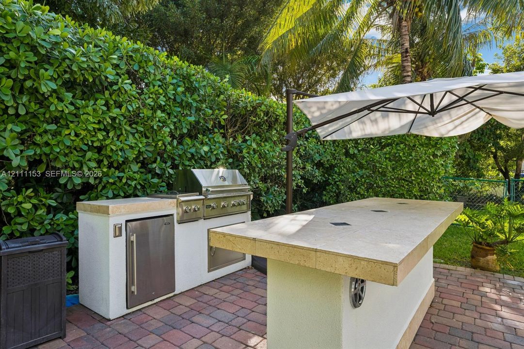 Outdoor kitchen featuring a built-in stainless steel grill, stone-finish countertop, integrated under-counter refrigeration, and paver patio flooring