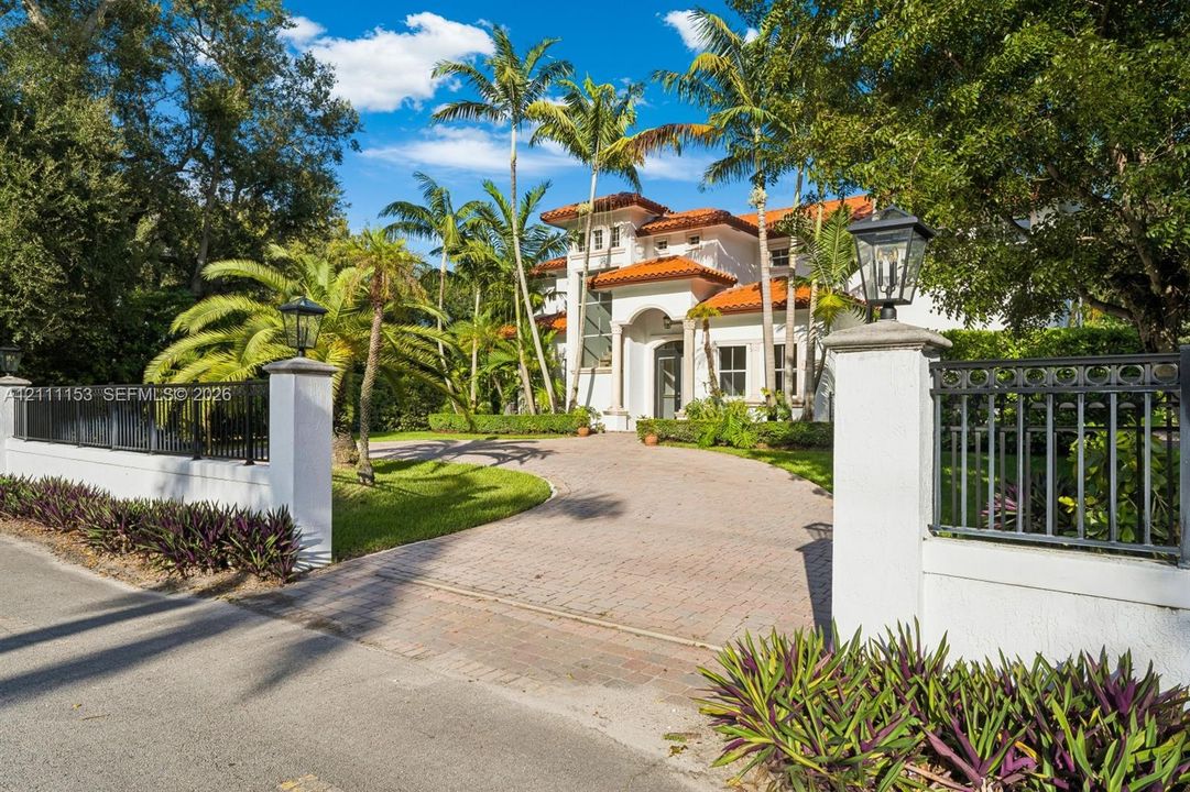 Mediterranean-style residence featuring a tile roof, stucco exterior, gated entrance with masonry pillars, and a paver driveway