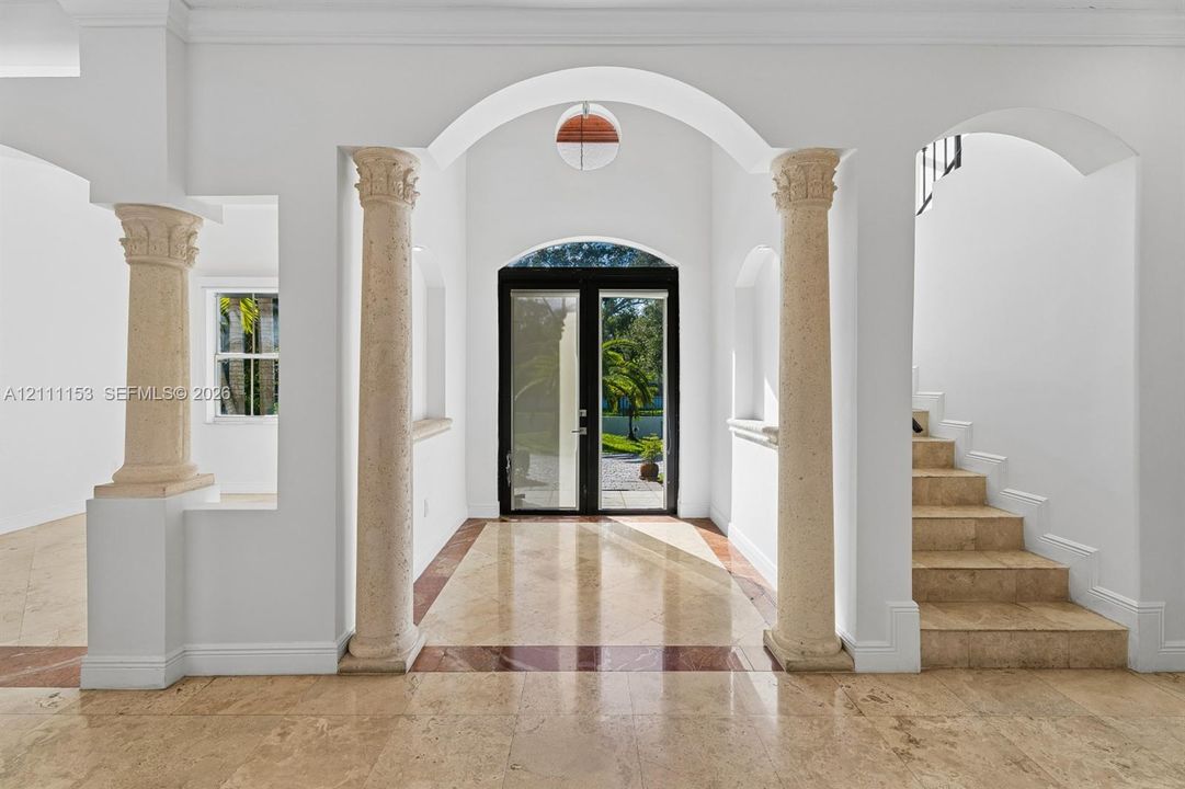 Grand foyer featuring stone columns, arched entryways, stone tile flooring with decorative inlay, and a multi-lite glass double door
