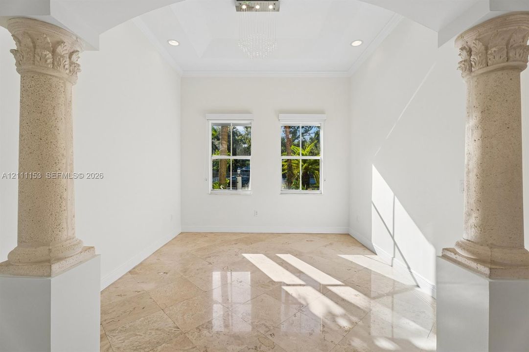 Architectural space defined by decorative stone columns, polished stone flooring, a tray ceiling with recessed lighting, and dual windows