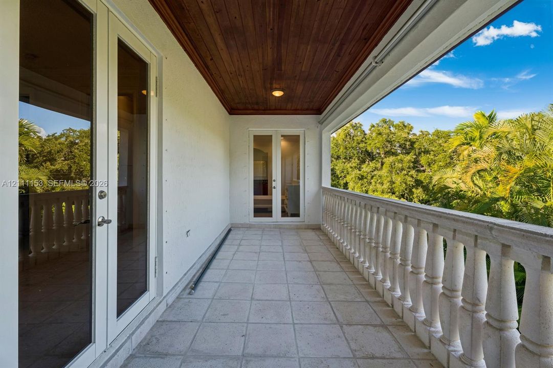 Covered balcony featuring a natural wood-finish plank ceiling, stone tile flooring, and a decorative stone balustrade with French door access