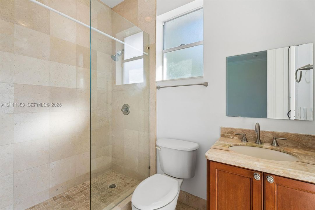 Bathroom featuring a walk-in shower with glass enclosure, natural stone wall tile, vanity with stone countertop, undermount sink, and wooden cabinetry