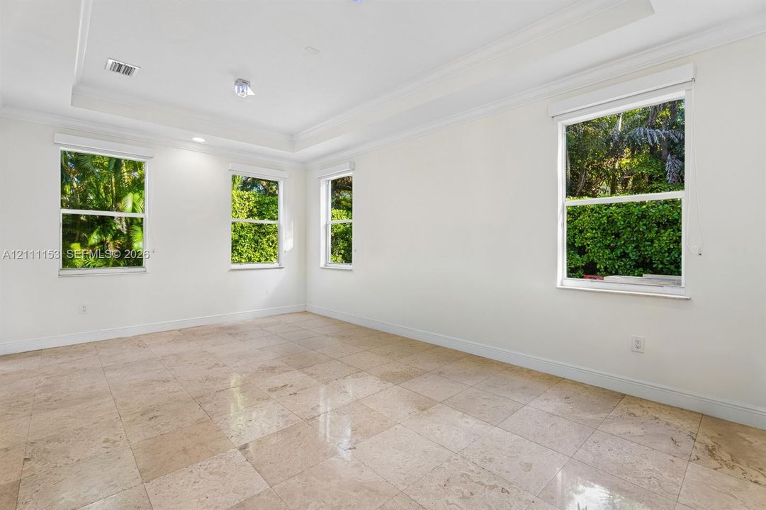 Spacious room featuring neutral tile flooring, a recessed tray ceiling, and four double-hung windows