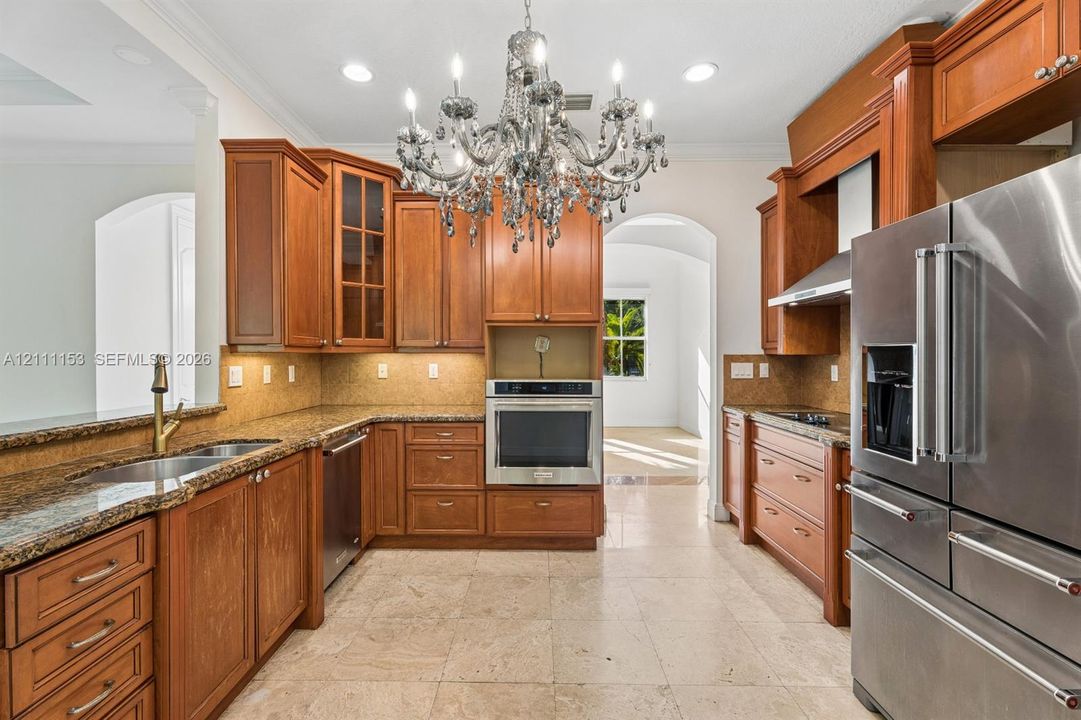 Kitchen featuring custom wood cabinetry, stone-surface countertops, built-in stainless steel appliances, a multi-tiered crystal chandelier, and large-format tile flooring