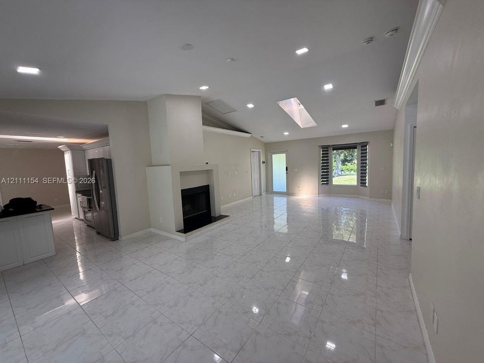 Open living area featuring vaulted ceilings, recessed lighting, a skylight, stone-finish tile flooring, and a fireplace with a custom hearth