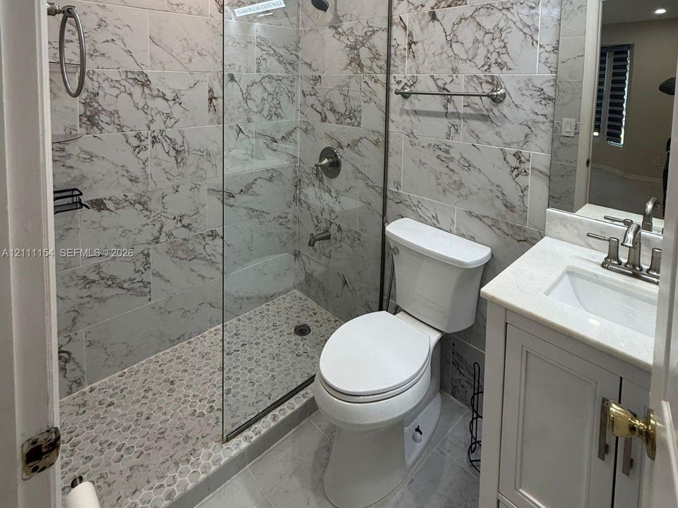 Bathroom featuring a glass-enclosed shower with stone-patterned wall tile and pebble-style floor tile, vanity with a stone countertop, and chrome fixtures