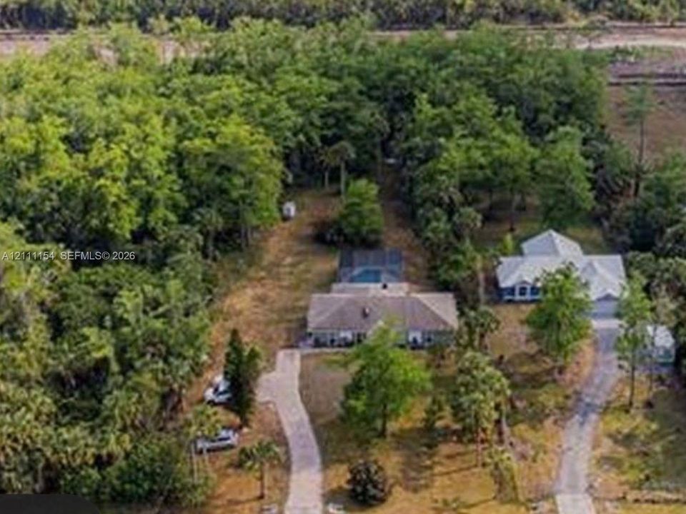 Aerial perspective of the property featuring a screened-in swimming pool, extensive wooded acreage, and paved private driveways