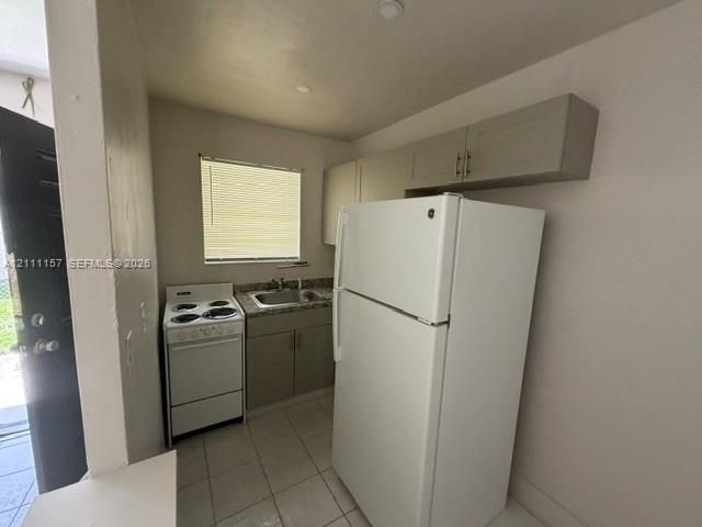 Kitchen featuring upper and lower cabinetry, stone-finish countertops, stainless steel sink with faucet, white electric range, and tiled flooring