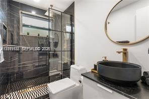 Full bathroom featuring a walk-in shower with a black grid glass partition, large-format dark stone-finish wall tile, geometric patterned floor tile, oval vessel sink, and brass-tone hardware