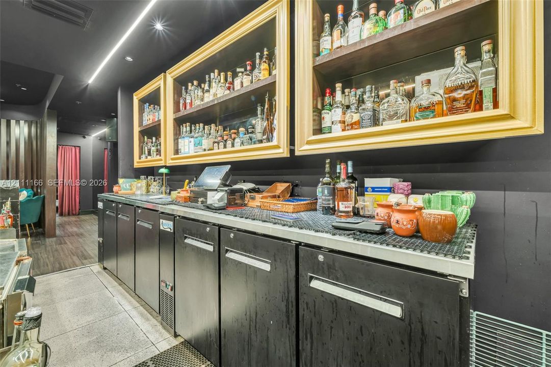 Built-in wet bar featuring black under-counter cabinetry, recessed wall shelving with gold-tone frames, and integrated linear lighting