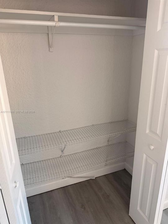 Closet featuring dual-panel doors, upper rod for garment hanging, two-tier white wire shelving, and wood-finish flooring