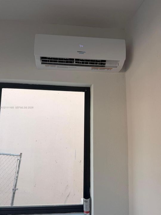 Wall-mounted mini-split climate control unit featuring a digital temperature display, paired with a dark-framed window