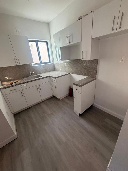 White flat-panel cabinetry featuring brushed metal hardware, speckled countertops, stainless steel sink with a swivel faucet, and wood-finish flooring