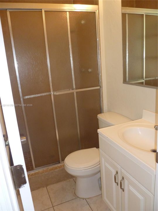 Shower featuring a metal-framed sliding enclosure with textured glass, single-basin vanity with an integrated countertop, wall-mounted mirror, and tile flooring