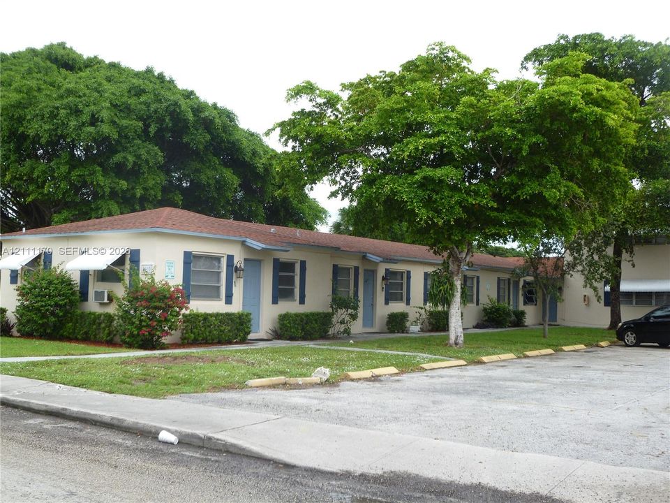 Single-story exterior featuring a hip roof, blue decorative shutters, assigned surface parking, and mature trees