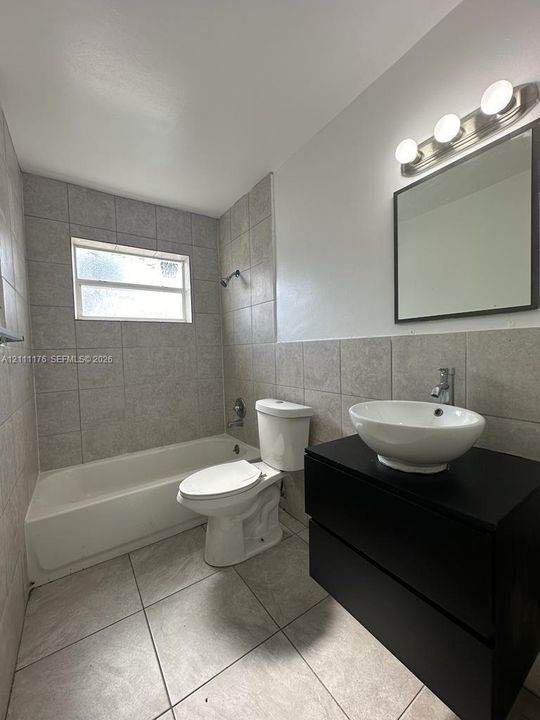 Black vanity featuring a vessel sink, ceramic tile flooring, full-height wall tiling in the shower area, and a wall-mounted light fixture