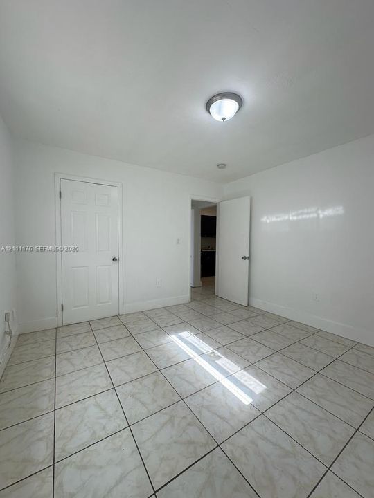 Neutral-toned tile flooring, white-painted walls, and two six-panel interior doors, illuminated by a flush-mount ceiling fixture