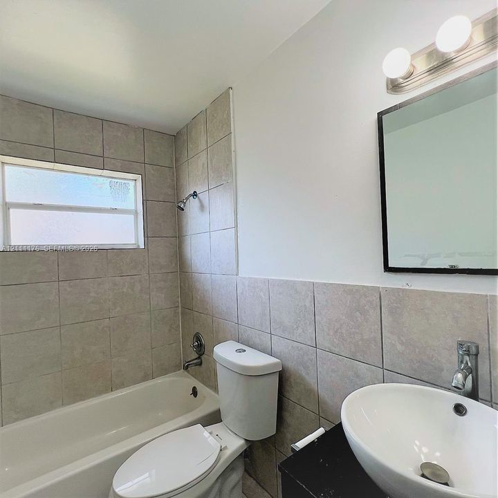 Bathroom featuring a tiled shower surround, vessel sink with a metal faucet, black countertop, wall-mounted mirror, and vanity lighting