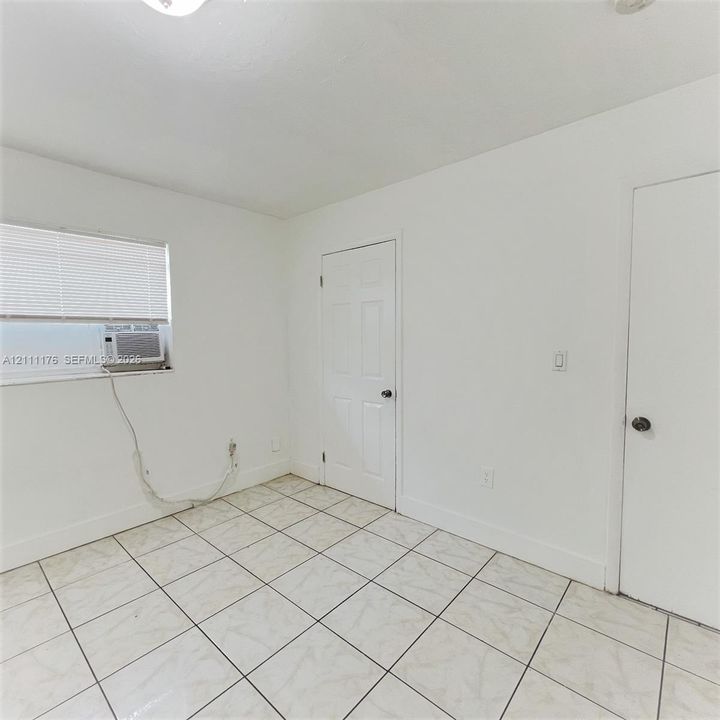 Room featuring white ceramic tile flooring, two six-panel interior doors, and a window with horizontal blinds
