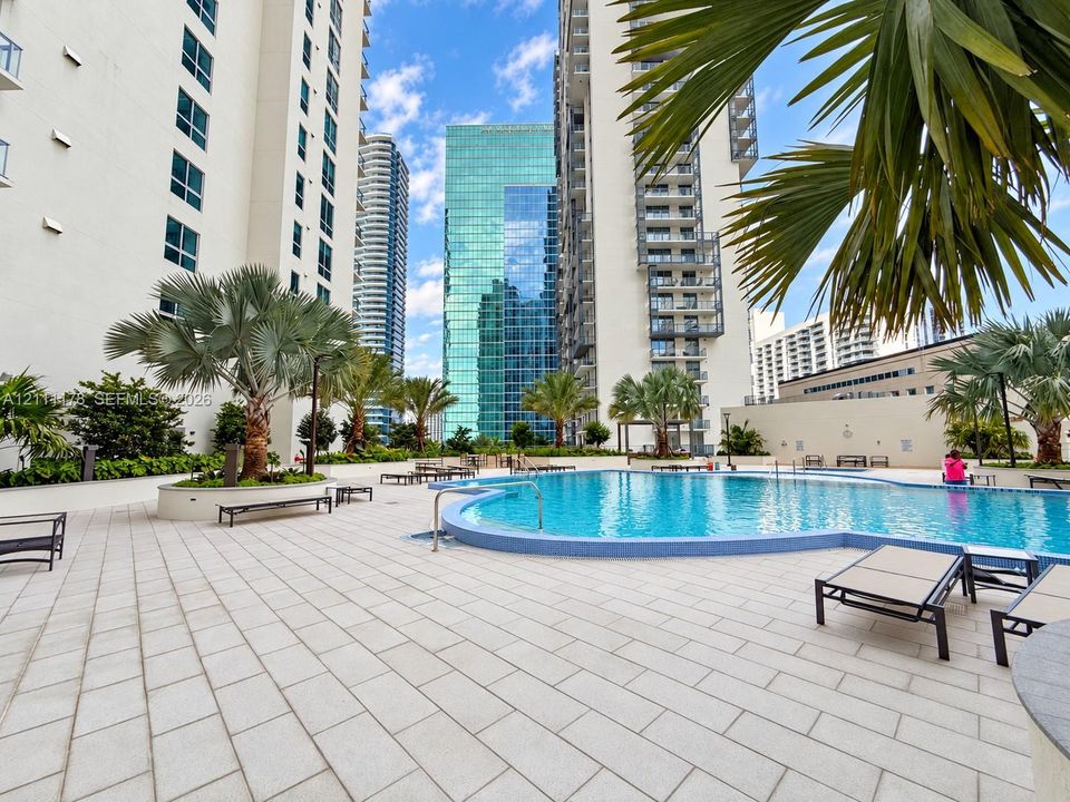 Swimming pool with tiled decking, surrounding landscaping, and high-rise exterior infrastructure