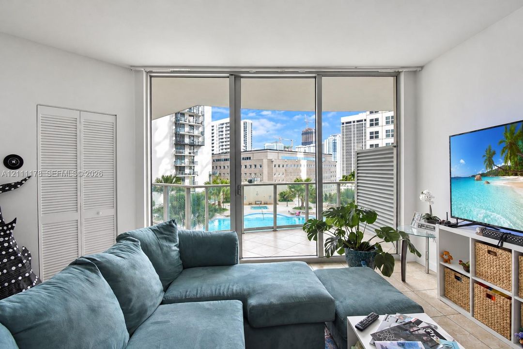 Floor-to-ceiling sliding glass doors, private balcony with metal railing, neutral tile flooring, and louvered double-door closet