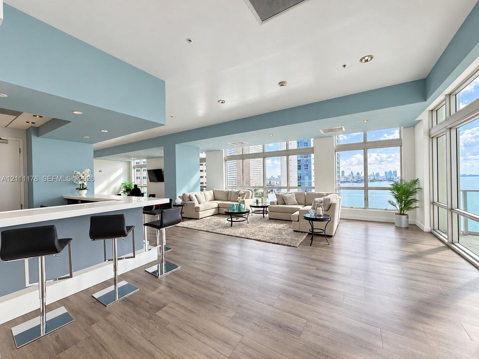 Open-concept living space featuring wood-finish flooring, floor-to-ceiling windows, a breakfast bar with stone-surface countertop, and recessed lighting