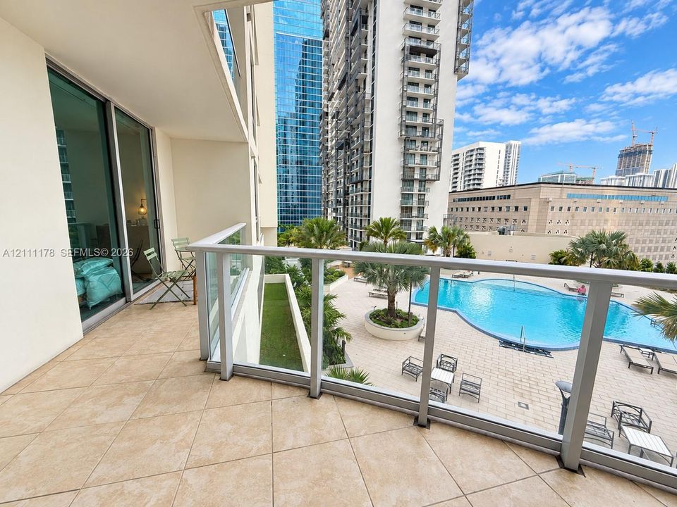 Private covered balcony featuring ceramic tile flooring, a glass panel railing with aluminum frame, and sliding glass entry doors