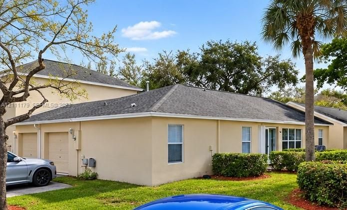 Stucco exterior with a multi-hipped asphalt shingle roof, attached two-car garage, and mature landscaping