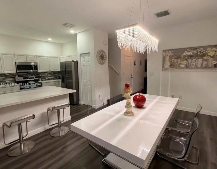 Kitchen featuring white cabinetry, a breakfast bar with stone-finish countertop, stainless steel appliances, a multi-tonal linear tile backsplash, and a rectangular crystal-accented chandelier