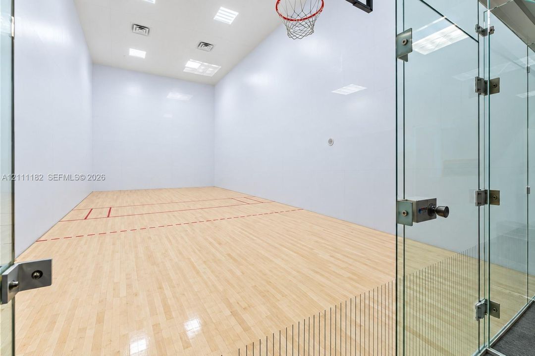 Recreational court featuring wood-finish flooring, high-impact walls, glass enclosure, and overhead recessed lighting