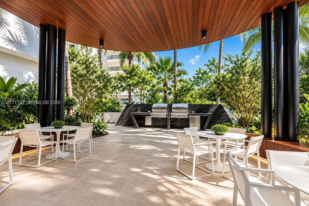 Covered outdoor kitchen featuring dual stainless steel grills, stone-finish countertops, wood-paneled ceiling, and large-format tile flooring