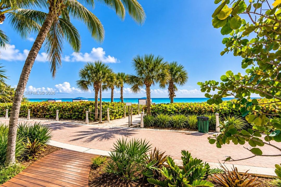 Paver walkway featuring mature palm trees, coastal landscaping, and wooden boardwalk accents