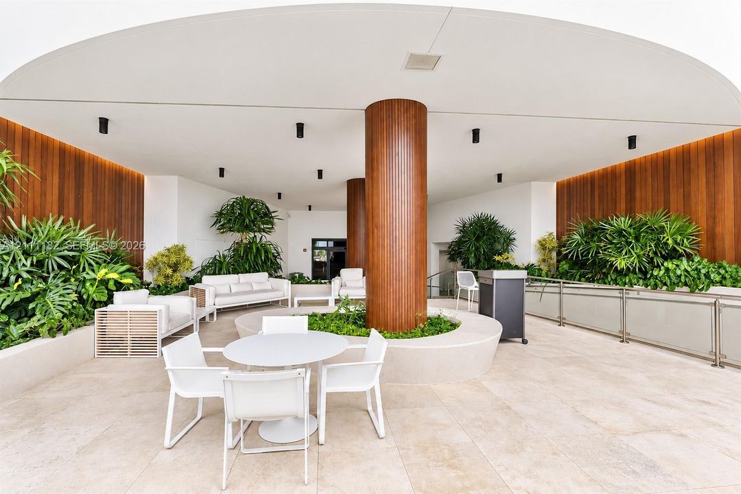 Covered outdoor terrace featuring large-format stone tile flooring, warm wood-paneled walls, integrated recessed lighting, and a central structural column with a circular built-in planter