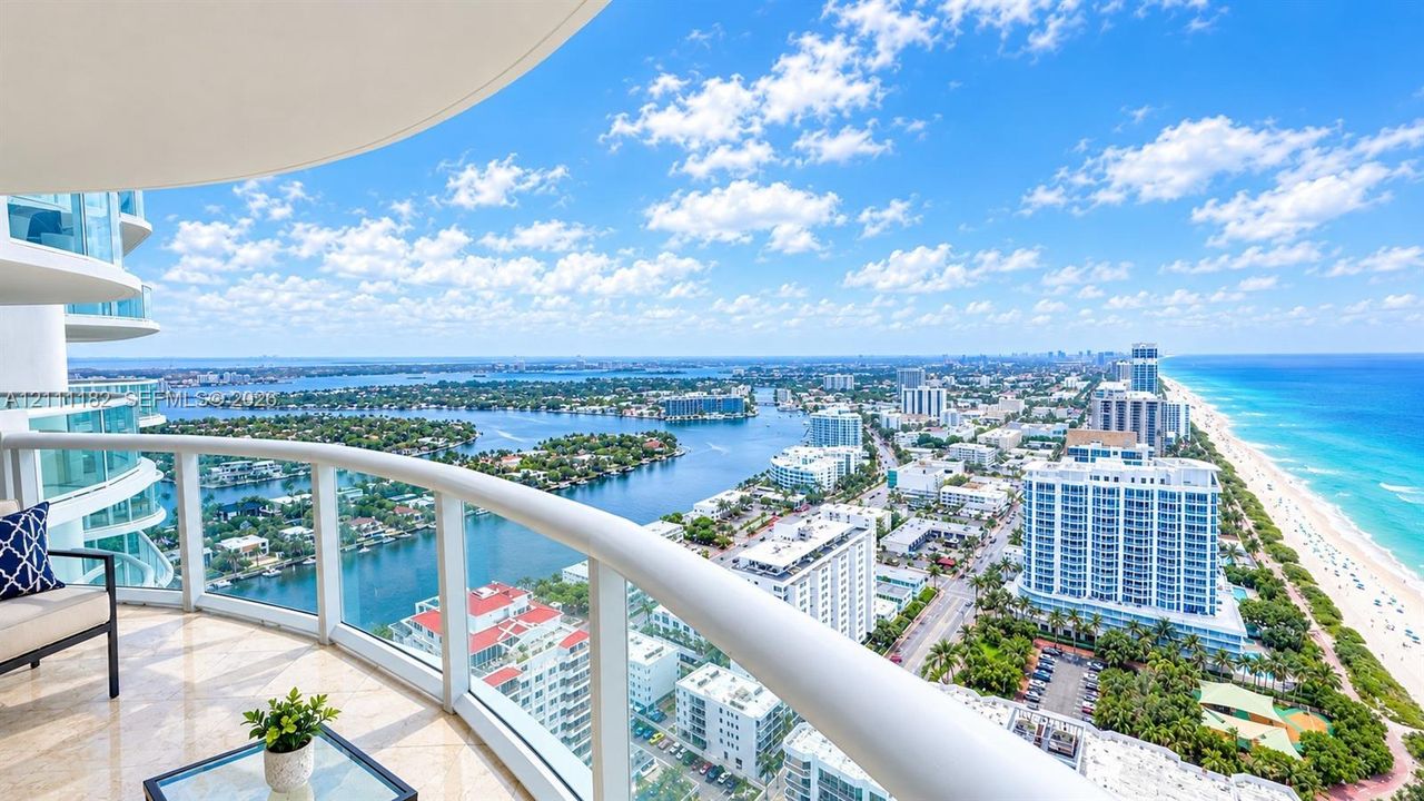 Curved covered balcony featuring stone flooring and glass-panel railings with expansive coastal and cityscape scenery