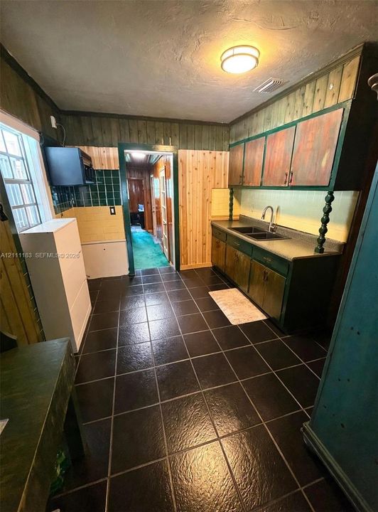 Kitchen featuring dark tile flooring, wood paneling, dual-basin sink, and wall-mounted cabinetry