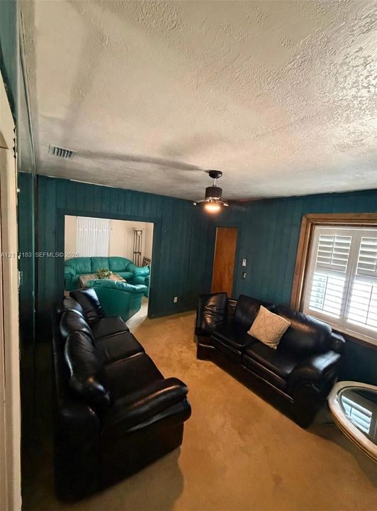 Wood-panel wall cladding, ceiling-mounted light fixture with fan, and window featuring interior plantation shutters