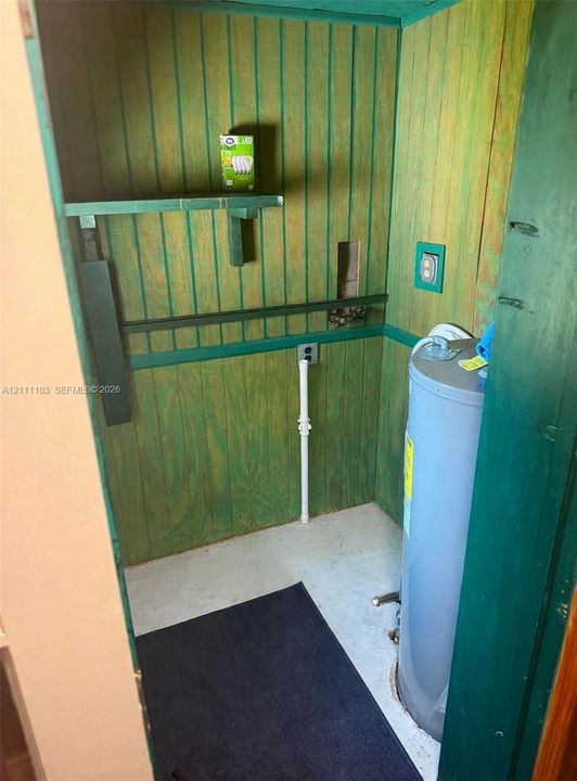 Vertical wood-paneled walls, built-in shelving, and an electric water heater