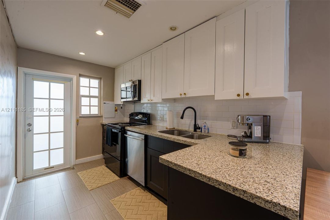 Kitchen featuring white upper cabinetry, dark lower cabinetry, speckled stone countertops, a white subway tile backsplash, and ceramic tile flooring
