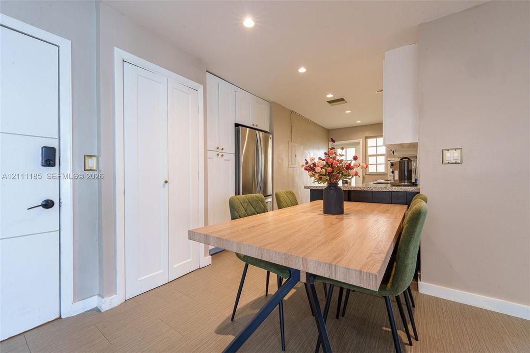 Kitchen area featuring white shaker-style cabinetry, stainless steel refrigerator, stone-surfaced island, and recessed lighting